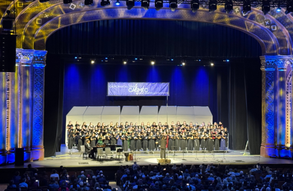 A large choir performs on stage in a theater, with a banner reading 'CALIFORNIA ALL-STATE CASMEC' above them.