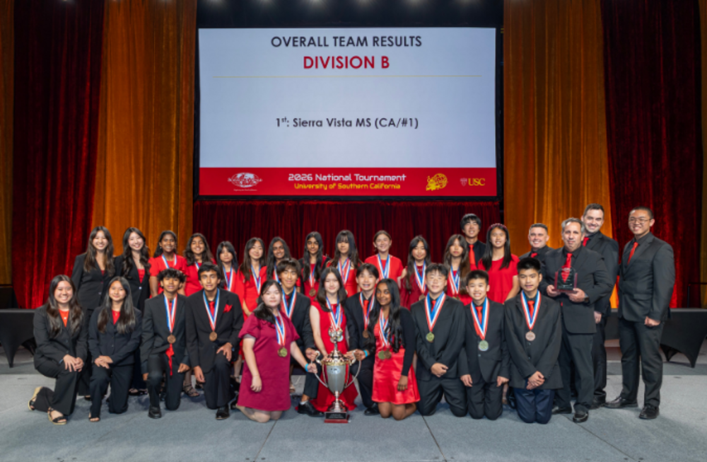 A group of students and adults in formal attire pose for a photo on stage, celebrating a first-place victory at the 2026 National Tournament.