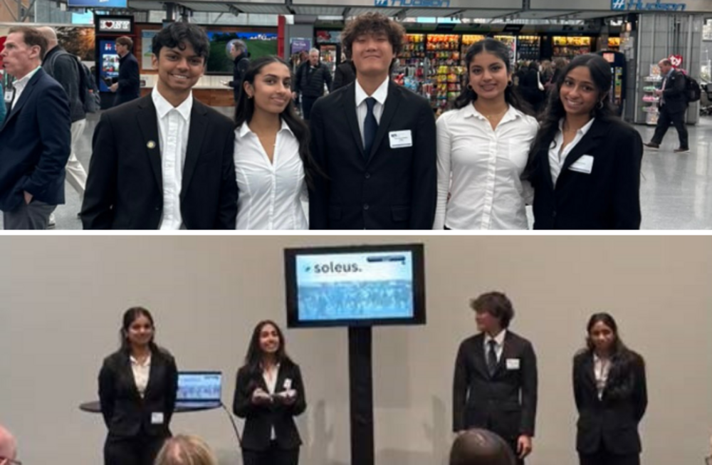 Four young people in suits stand together in a public space with shops in the background.
