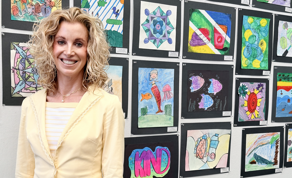IUSD Superintendent Cassie Parham stands in front of a student artwork display featuring colorful drawings and paintings mounted on a wall.