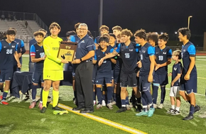 A soccer team celebrates on a field at night, holding a championship trophy.