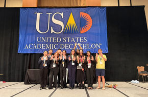 Uni's Academic Decathlon team pose for a photo in front of a United States Academic Decathlon banner.