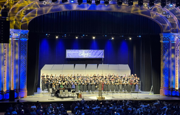 A large choir performs on stage in a theater, with a banner reading 'CALIFORNIA ALL-STATE CASMEC' above them.