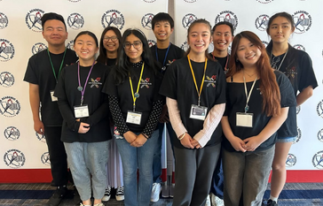 A group of smiling students in black t-shirts stand together, posing for a photo.