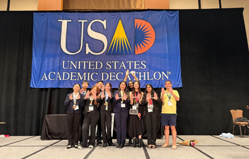 Uni's Academic Decathlon team pose for a photo in front of a United States Academic Decathlon banner.