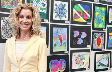 IUSD Superintendent Cassie Parham stands in front of a student artwork display featuring colorful drawings and paintings mounted on a wall.