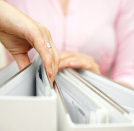 A person in a pink shirt searches through a row of white binders filled with documents