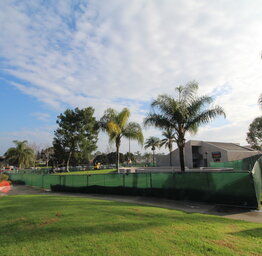 A wide shot of a green construction fence stretching across Lakeside MS courtyard under a blue, cloudy sky.