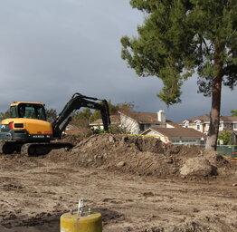 A Hyundai excavator working on a dirt pile in front of Lakeside MS with residential houses in the background.