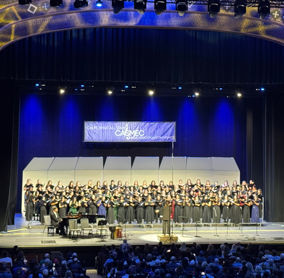 A large choir performs on stage in a theater, with a banner reading 'CALIFORNIA ALL-STATE CASMEC' above them.