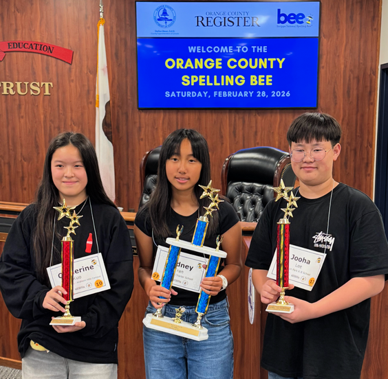 Three students proudly hold trophies after a spelling bee competition.