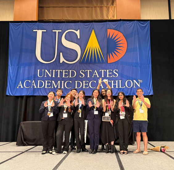Uni's Academic Decathlon team pose for a photo in front of a United States Academic Decathlon banner.