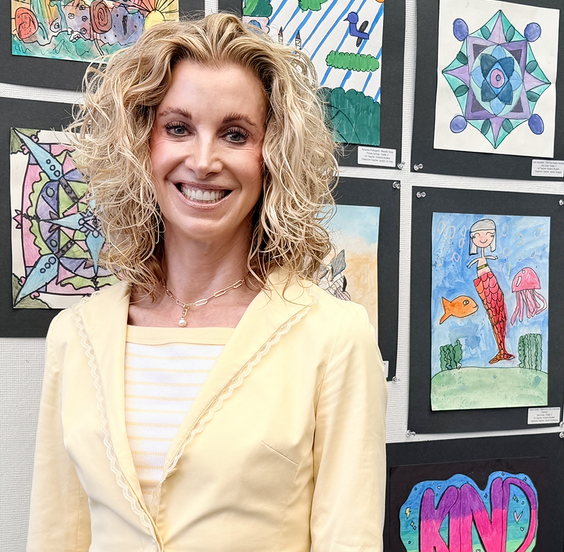IUSD Superintendent Cassie Parham stands in front of a student artwork display featuring colorful drawings and paintings mounted on a wall.
