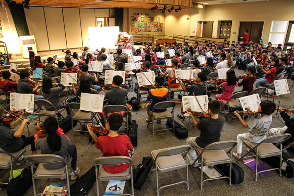 Stonegate student orchestra practicing in a spacious room with music stands and chairs.
