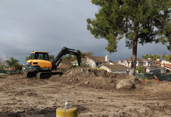 A Hyundai excavator working on a dirt pile in front of a residential neighborhood.