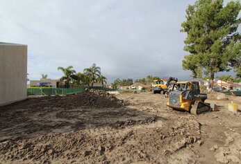Wide view of a muddy construction site featuring a John Deere loader and a Hyundai excavator.