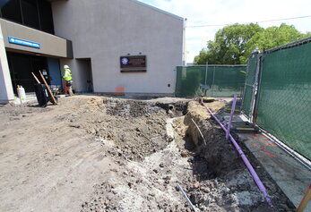 A close-up view of a freshly dug trench and exposed purple utility pipes next to a building marked as a California Distinguished School.