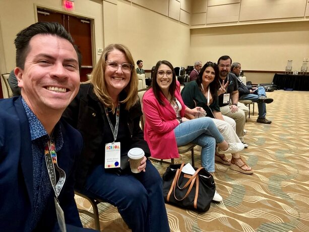 IUSD staff sit in chairs in a conference room, smiling.