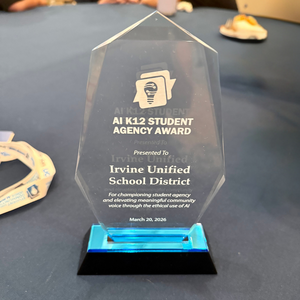 A clear acrylic award with blue accents, recognizing the 'AI K12 STUDENT AGENCY AWARD' presented to Irvine Unified School District.