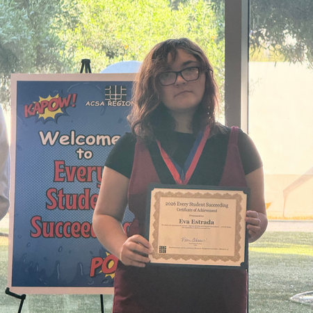 Eva Estrada holding award in front of event welcome banner